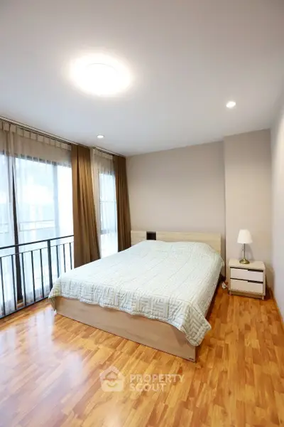 Spacious bedroom with large windows and wooden flooring in modern apartment.