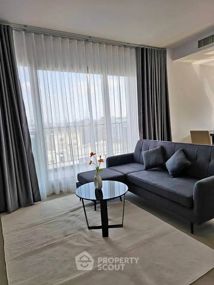 Elegant living room with modern sofa and glass coffee table, featuring floor-to-ceiling windows and sheer curtains.