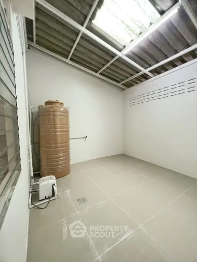 Spacious utility room with water tank and tiled flooring, ideal for storage or laundry setup.