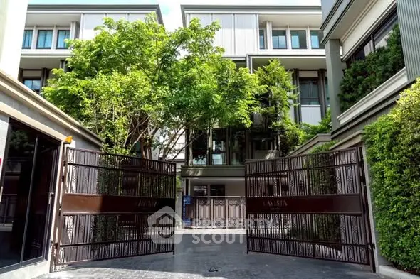 Modern gated entrance to luxury residential building with lush greenery.