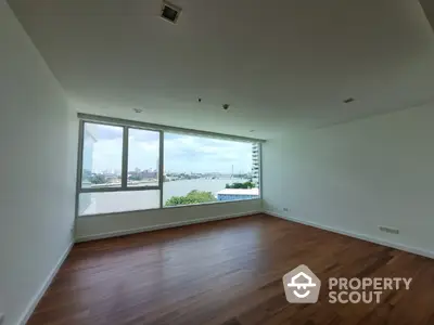 Spacious living room with hardwood floors and expansive windows offering a stunning view of the waterfront, perfect for entertaining or relaxing.