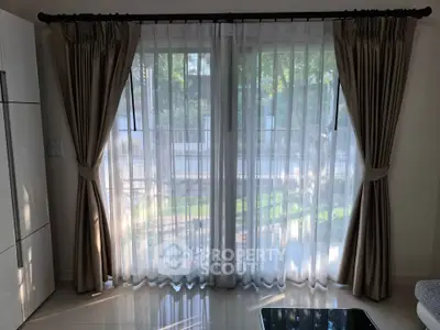 Elegant living room with large window and stylish curtains offering a serene garden view.