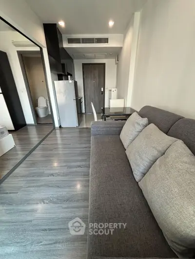 Modern apartment interior with sleek gray sofa and compact kitchen area.