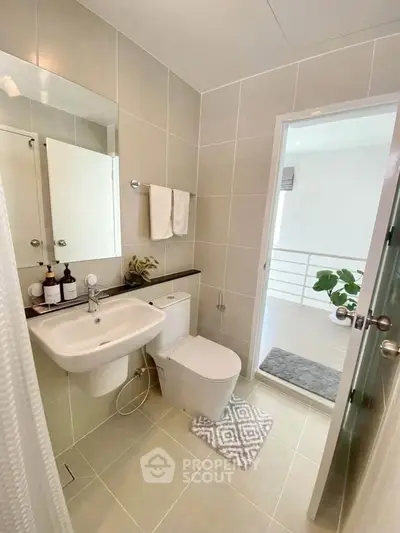 Modern bathroom with sleek fixtures and neutral tiles, featuring a white sink and toilet.