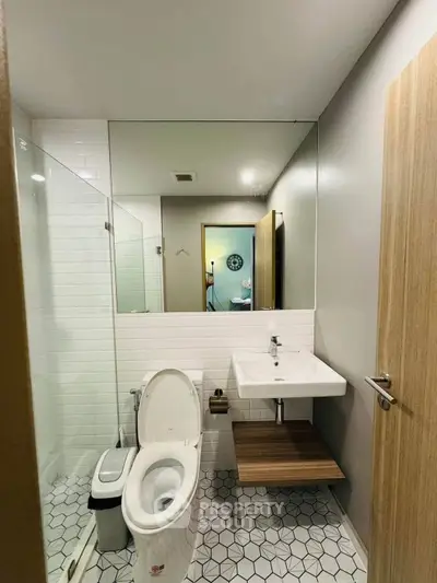 Modern bathroom with sleek fixtures and geometric tile flooring, featuring a glass shower and wall-mounted sink.