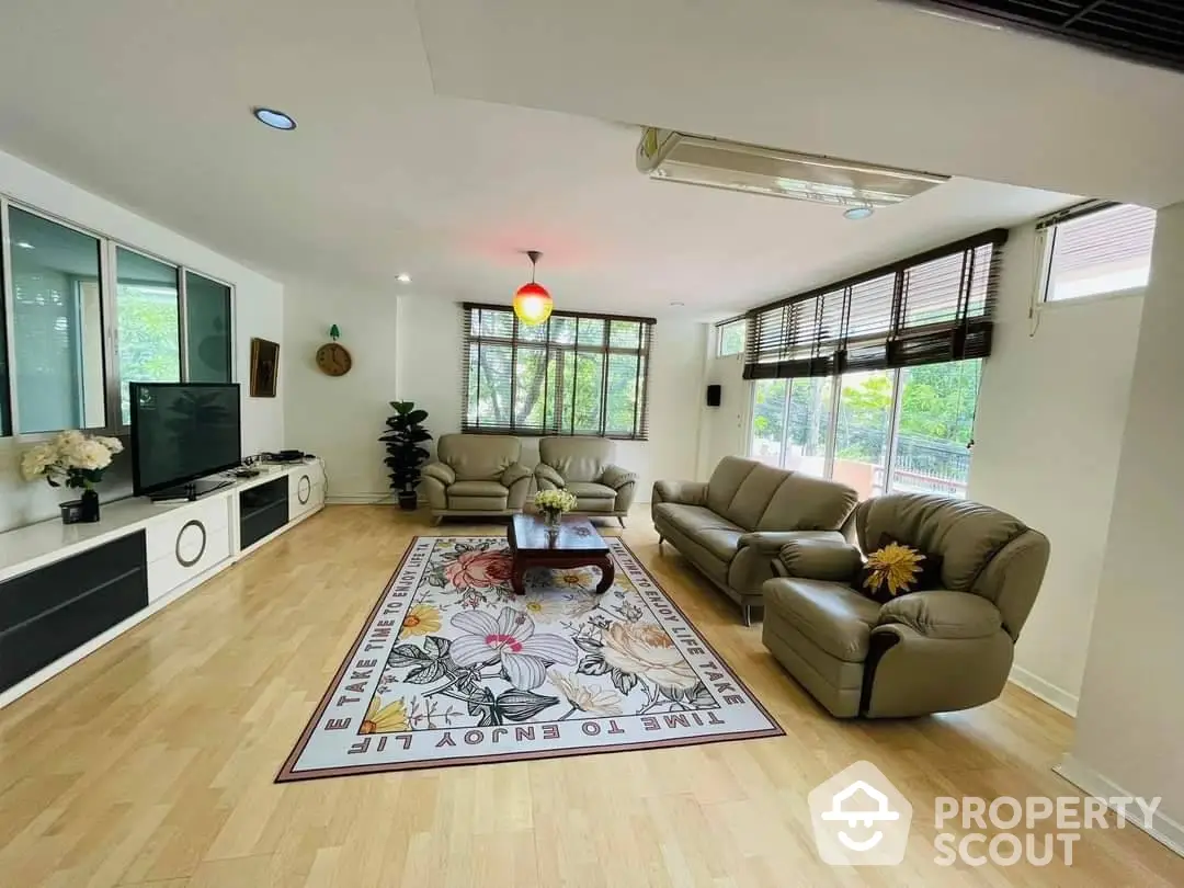 Spacious living room with ample natural light, modern furniture, and a vibrant area rug, perfect for family gatherings and relaxation.