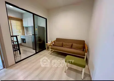 Cozy living room with modern kitchen view, featuring sleek glass partition and stylish furniture.