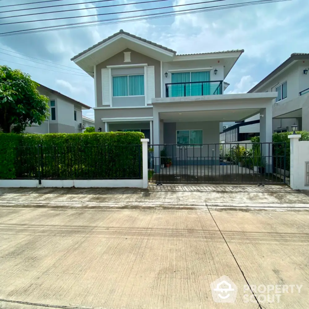 Modern two-story house with balcony and lush greenery in a serene neighborhood.