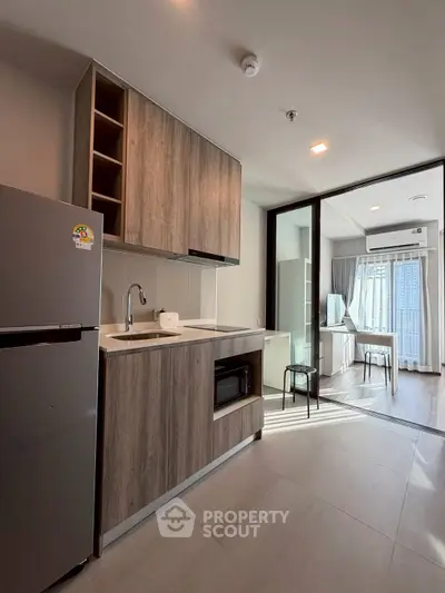 Modern kitchen with wooden cabinets and open layout leading to bright living area.
