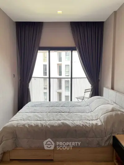 Cozy bedroom with modern decor and large window overlooking balcony in urban apartment.