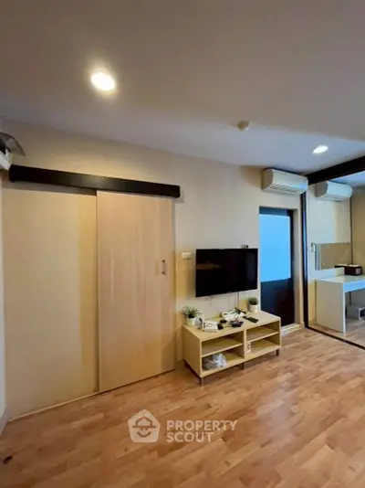 Modern living room with wooden flooring, sliding door, and wall-mounted TV in a cozy apartment.