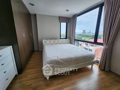 Spacious bedroom with large windows offering stunning city views and elegant wooden flooring.