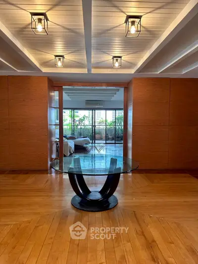 Luxurious interior with elegant glass table and wooden flooring leading to a spacious balcony.