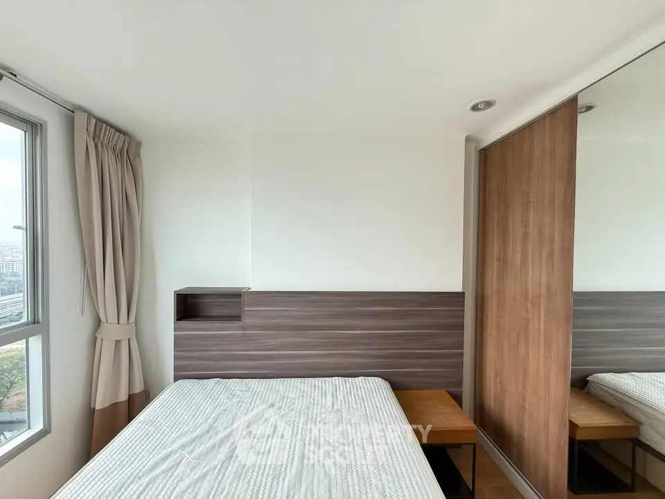 Modern bedroom with large window and built-in wardrobe in a high-rise apartment.