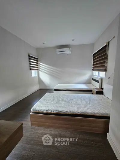 Spacious bedroom with two beds and modern air conditioning unit, featuring elegant window blinds and wooden flooring.