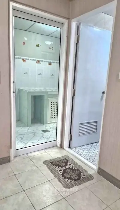 Modern bathroom with glass door and tiled flooring, featuring a sleek design and functional layout.