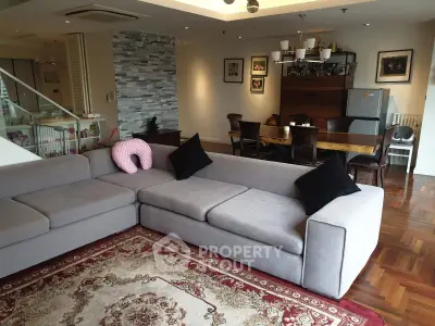 Spacious living room with modern decor and elegant dining area, featuring a plush gray sofa and stylish lighting.