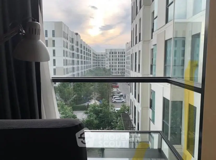 Modern apartment view with large windows overlooking a contemporary building complex and lush greenery.