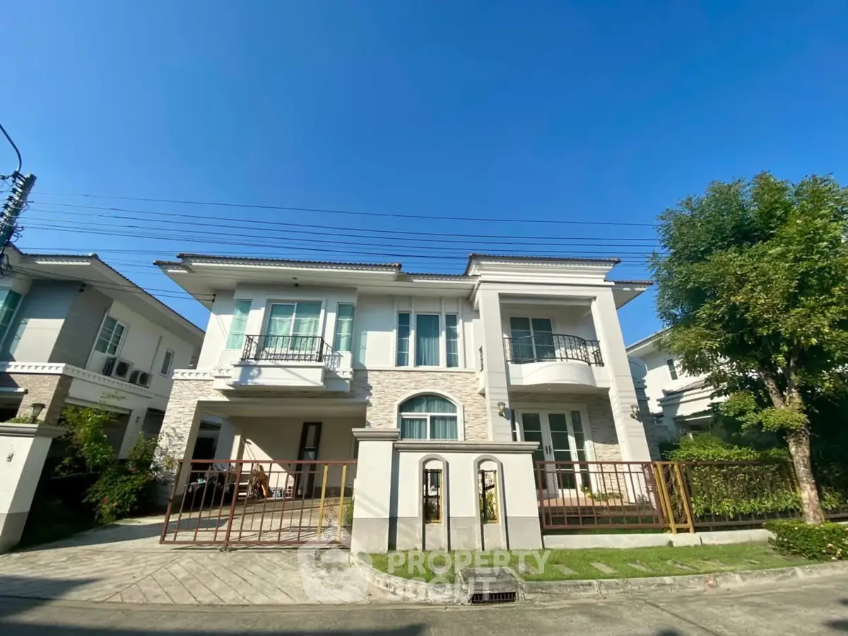Elegant two-story house with balconies and lush greenery in a serene neighborhood.