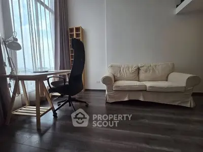 Modern living room with cozy sofa and stylish desk setup, featuring large windows and wooden flooring.