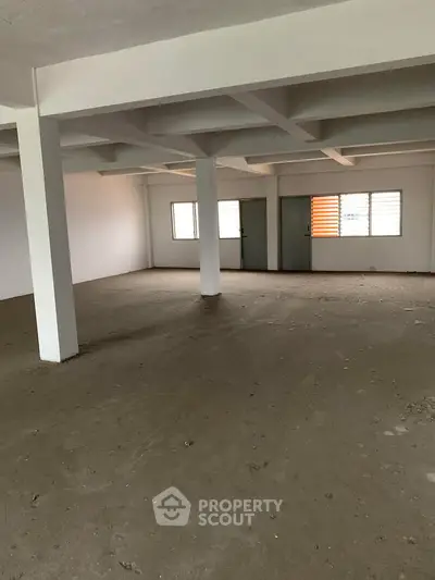 Spacious unfinished commercial space with concrete flooring and large windows.