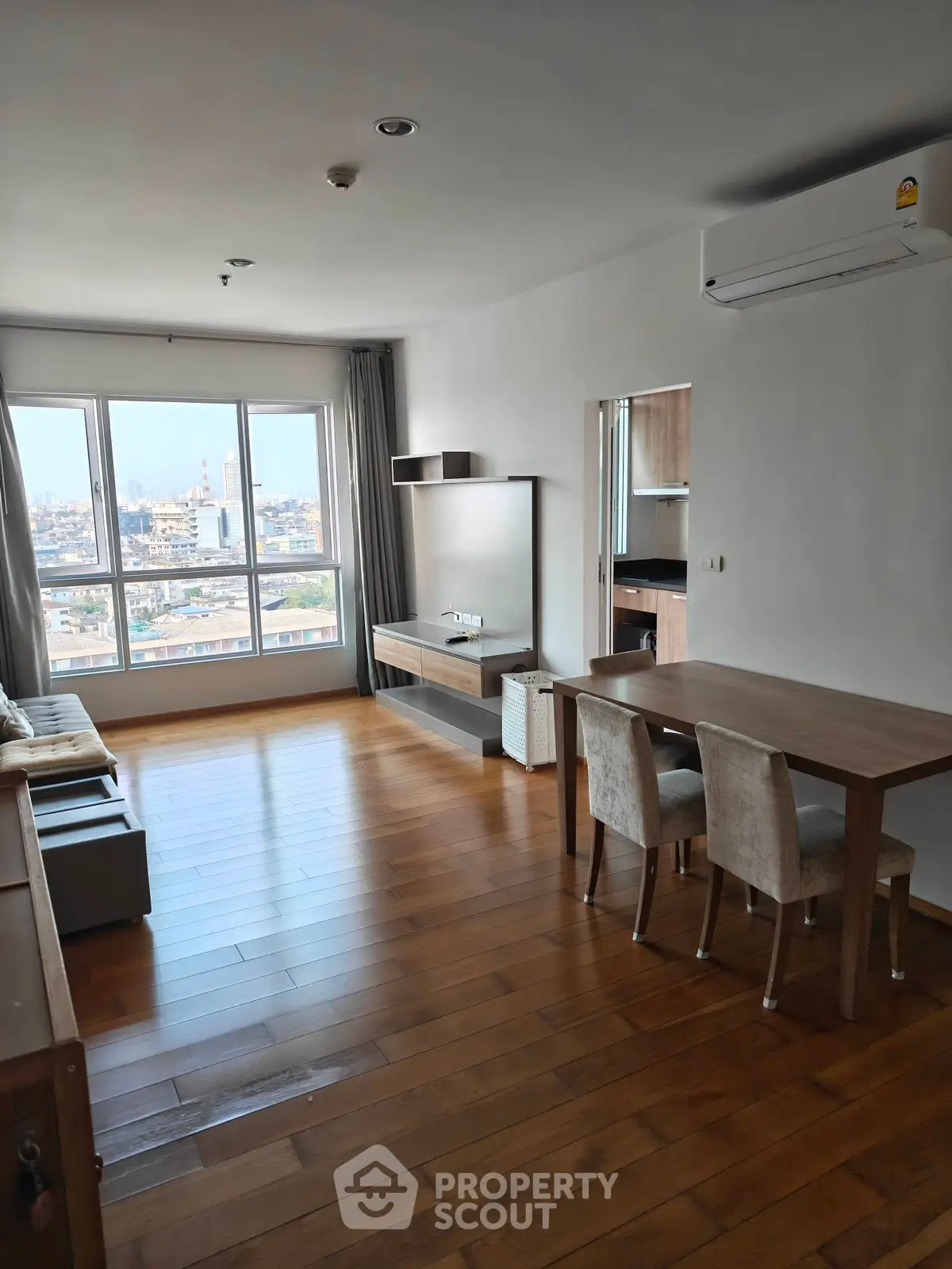 Modern living room with wooden flooring and city view, featuring sleek furniture and air conditioning.
