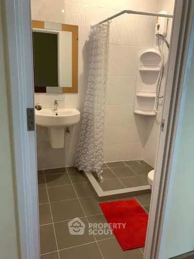 Modern bathroom with shower, sink, and red mat, ideal for compact living spaces.