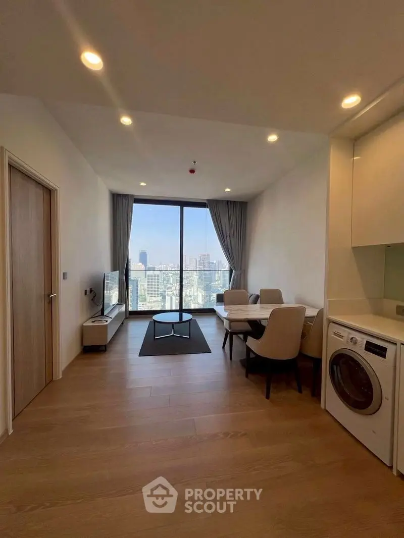 Modern living room with city view, featuring dining area and in-unit washer.