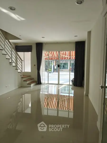 Spacious modern living room with large windows and staircase, perfect for natural light.