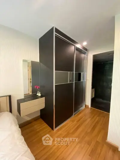 Modern bedroom with sleek wardrobe and wooden flooring, featuring a stylish vanity area.