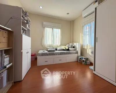 Cozy bedroom with wooden flooring, built-in storage, and natural light from large windows.