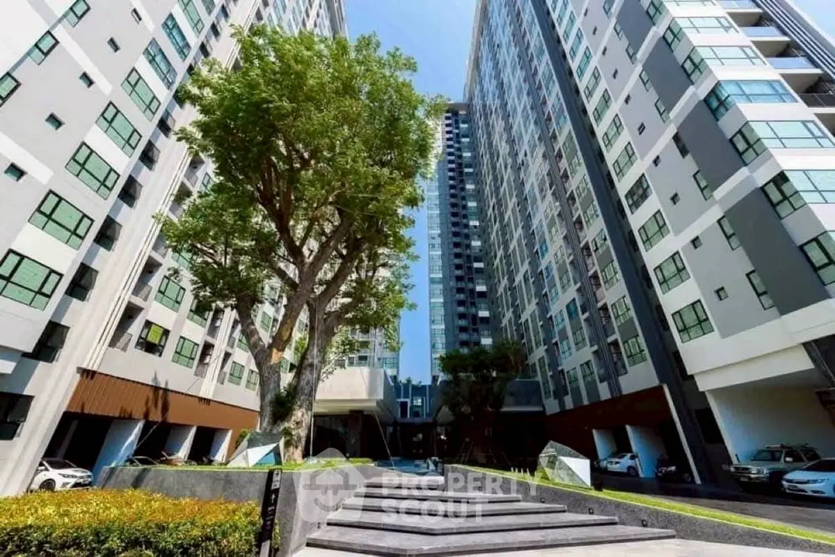 Modern high-rise residential building with lush greenery and spacious entrance.