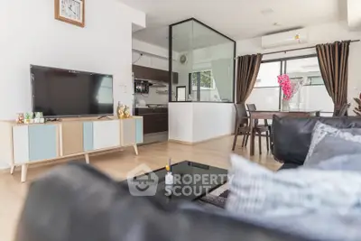 Modern living room with stylish decor and open kitchen layout, featuring a large TV and elegant dining area.