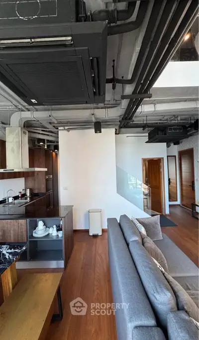 Modern industrial-style living room with open kitchen and sleek furnishings.