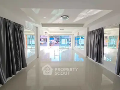 Spacious sunlit room with large windows and elegant curtains, perfect for versatile use.