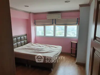Cozy bedroom with pink walls, large window, and air conditioning unit in a city apartment.