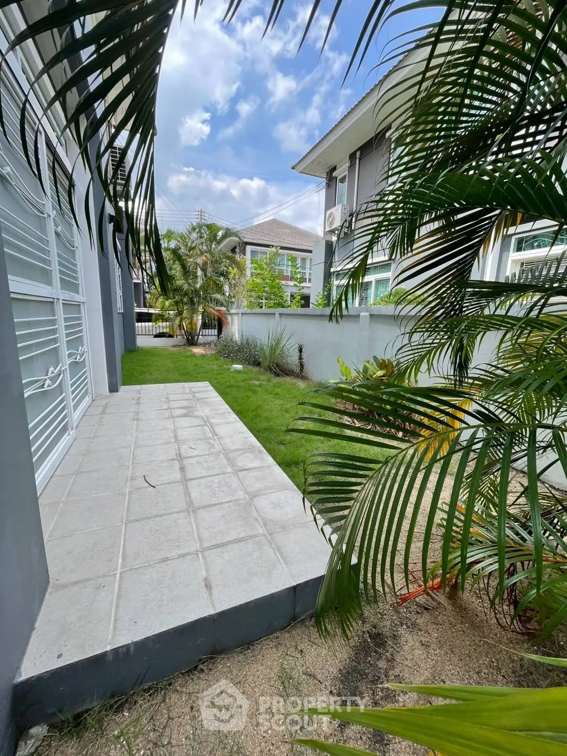 Charming garden view of modern residential building with lush greenery and tiled patio.