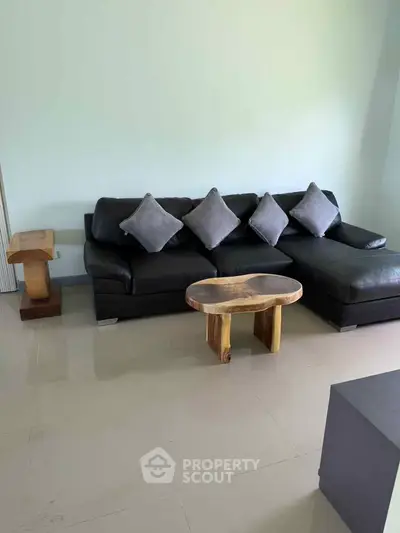 Modern living room with sleek black leather sofa and stylish wooden coffee table.