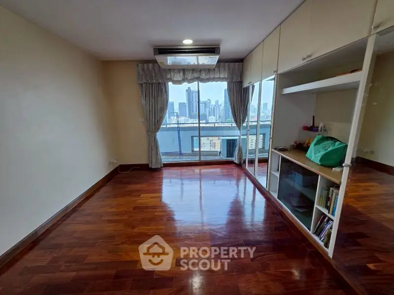 Spacious room with polished wooden floors and city view from large window.