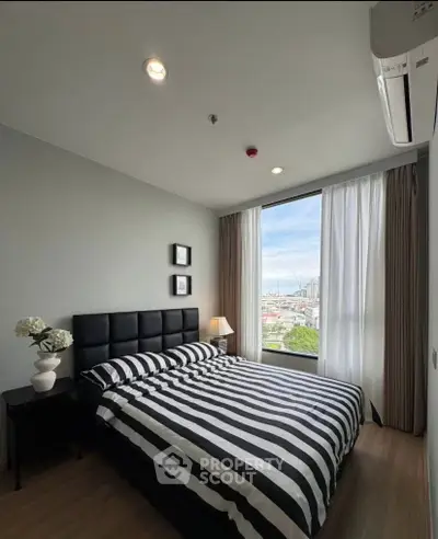 Modern bedroom with striped bedding and large window offering city view