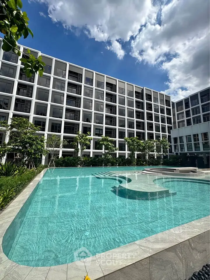 Luxurious modern apartment complex with stunning outdoor pool and lush greenery under a clear blue sky.