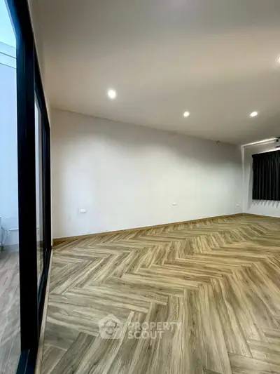 Spacious modern living room with elegant herringbone wood flooring and recessed lighting.