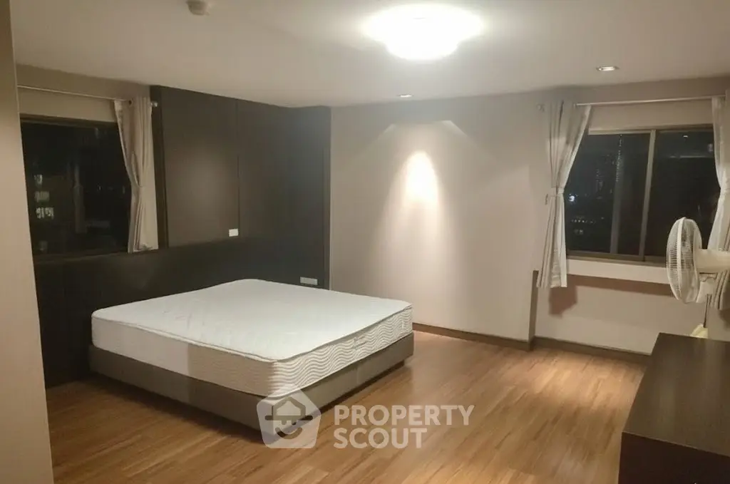 Spacious bedroom with wooden flooring and large windows for natural light.