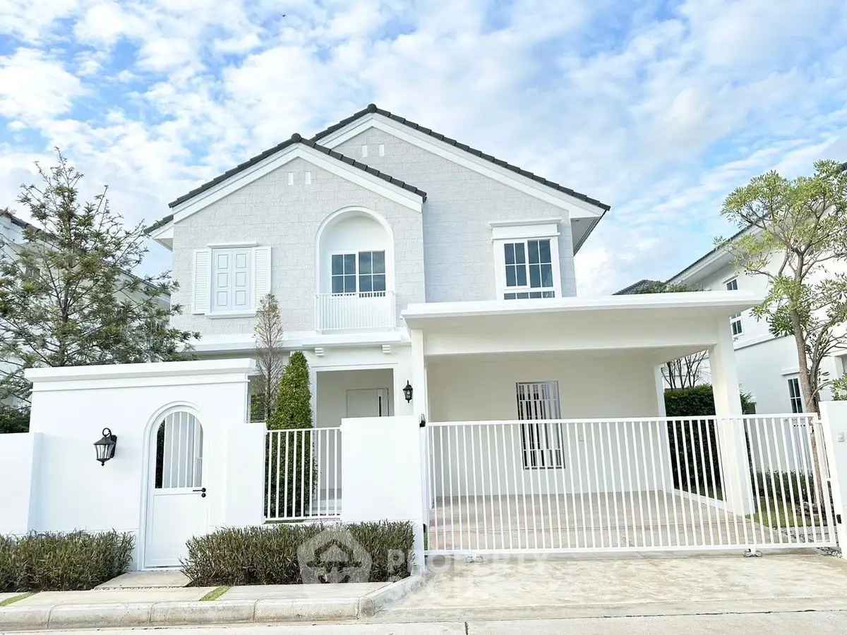 Elegant two-story white house with gated entrance and lush greenery