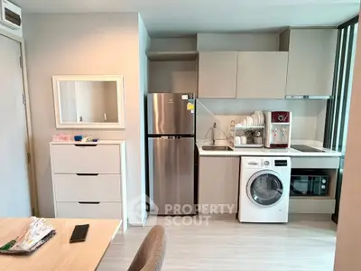 Modern kitchen with stainless steel fridge, washing machine, and microwave in compact layout.