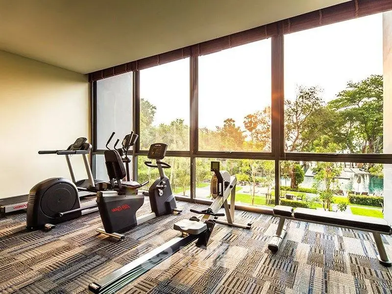 Modern gym with large windows offering scenic garden views, equipped with exercise machines.