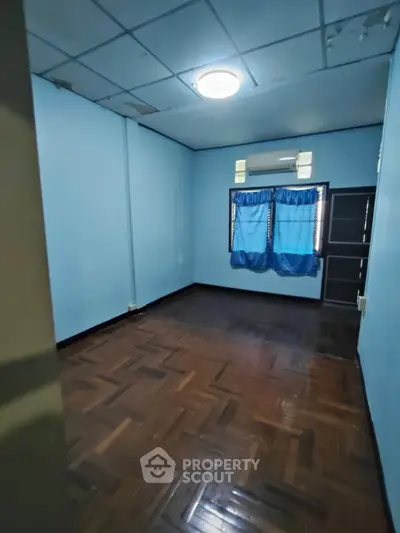 Spacious empty room with wooden flooring and blue walls, ideal for customization.