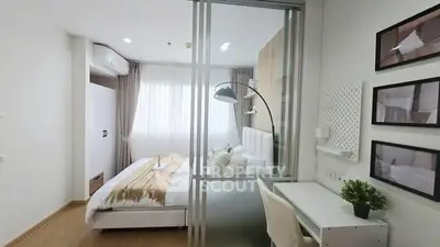 Modern bedroom with glass partition and study area, featuring sleek decor and natural light.