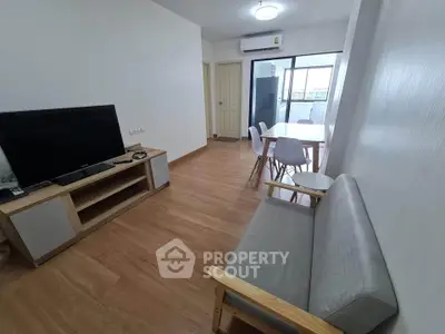 Modern living room with sleek furniture and wooden flooring, featuring a TV and dining area.