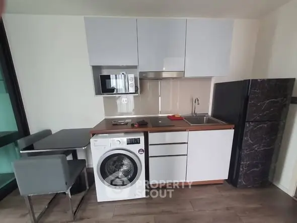 Modern compact kitchen with washing machine and sleek appliances in a stylish apartment.